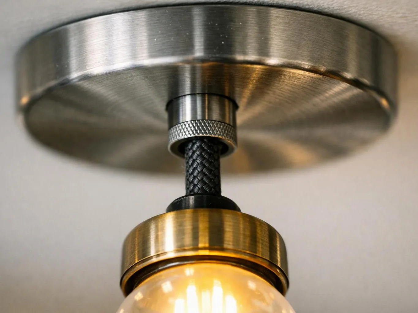 A brass ceiling light hangs from a braided black cord and glows warmly against a plain ceiling