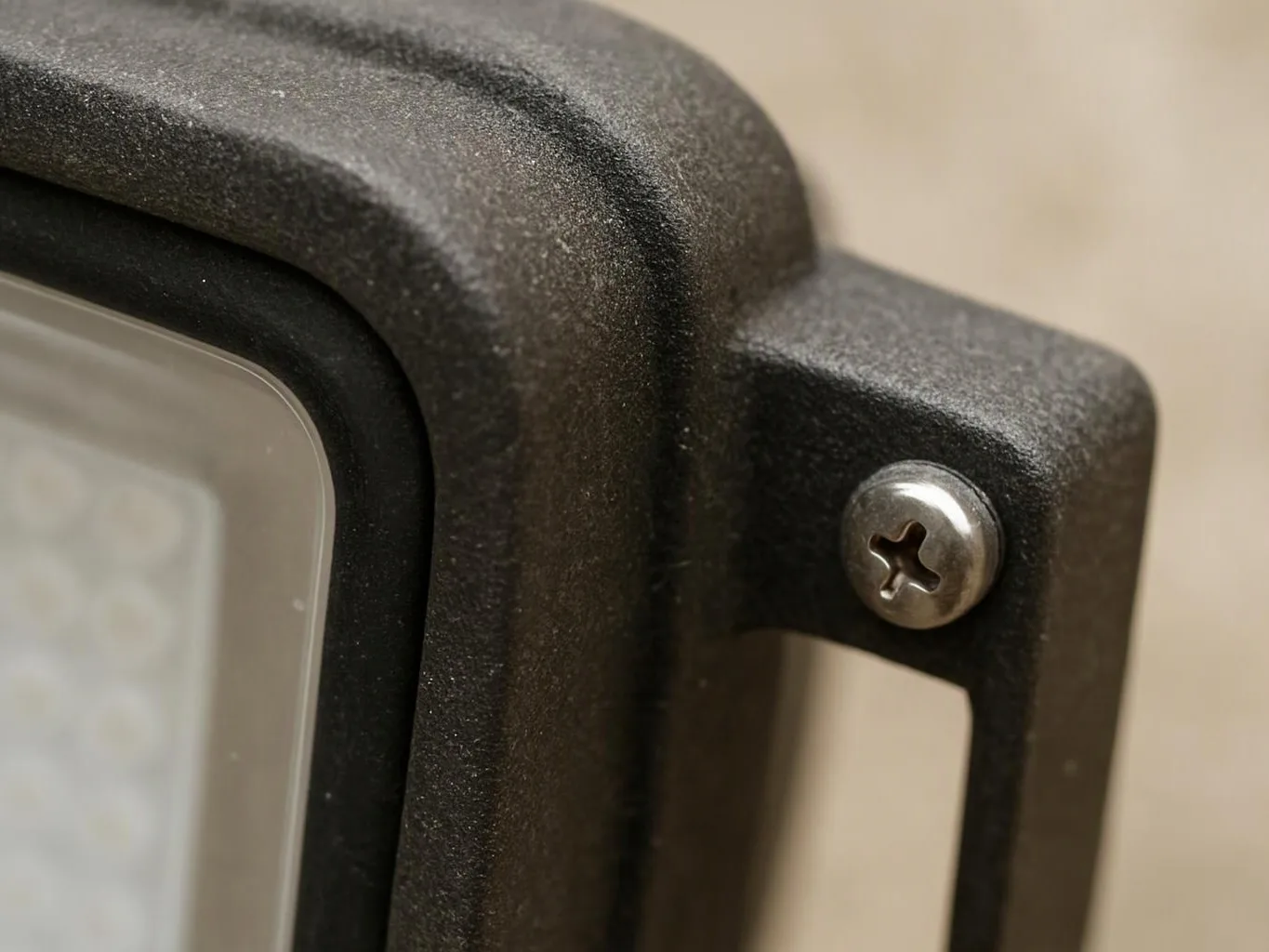 Close-up of a black plastic light fixture with a silver screw against a beige wall