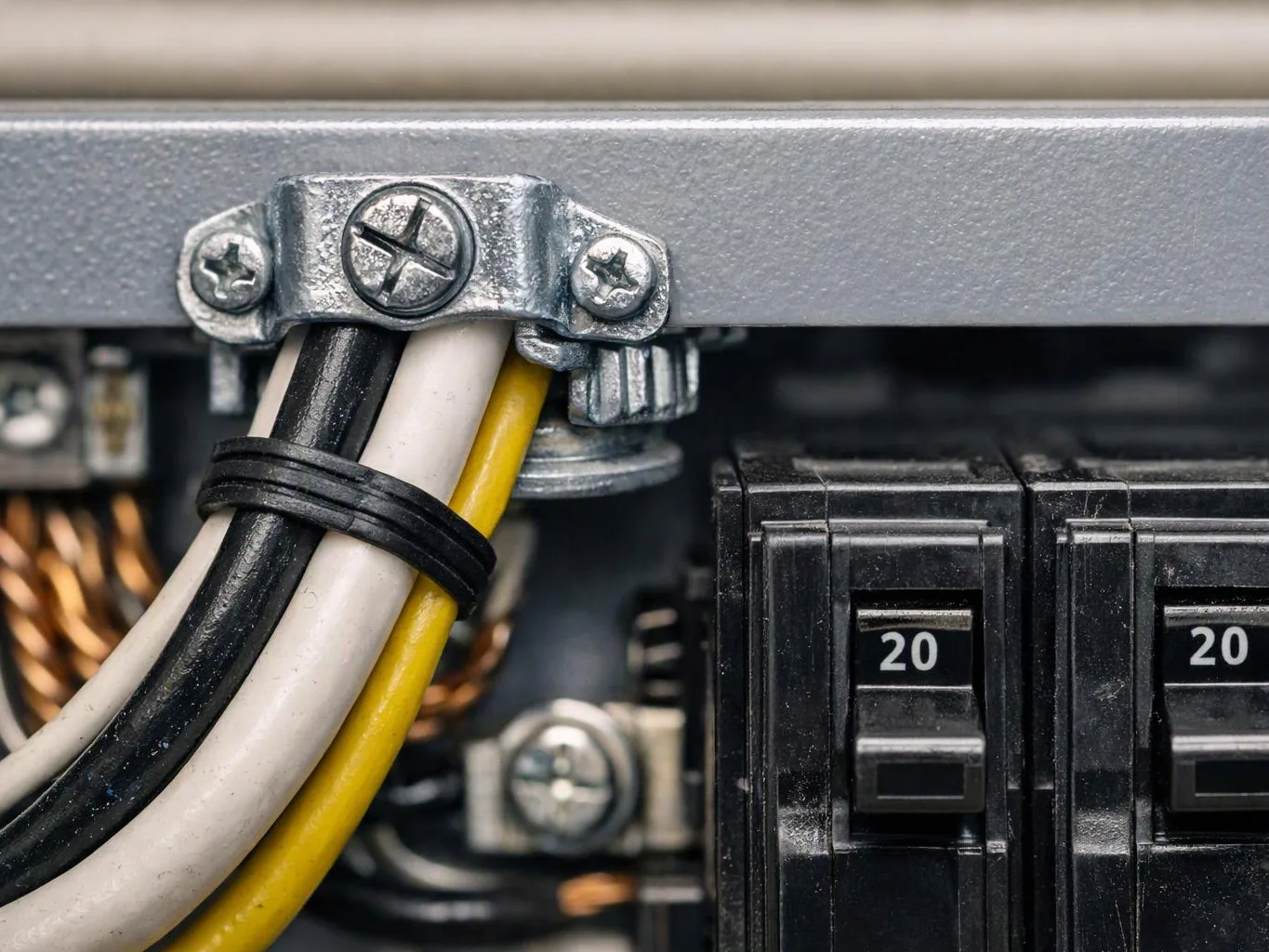 Close-up of electrical wiring beside two black circuit breakers labeled 20 inside a metal panel