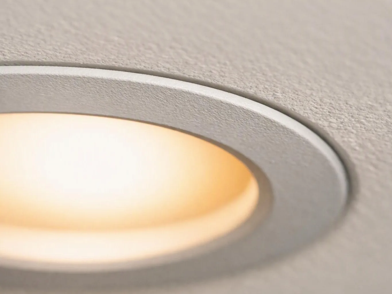 Close-up of a recessed ceiling light glowing warm white against a textured gray surface