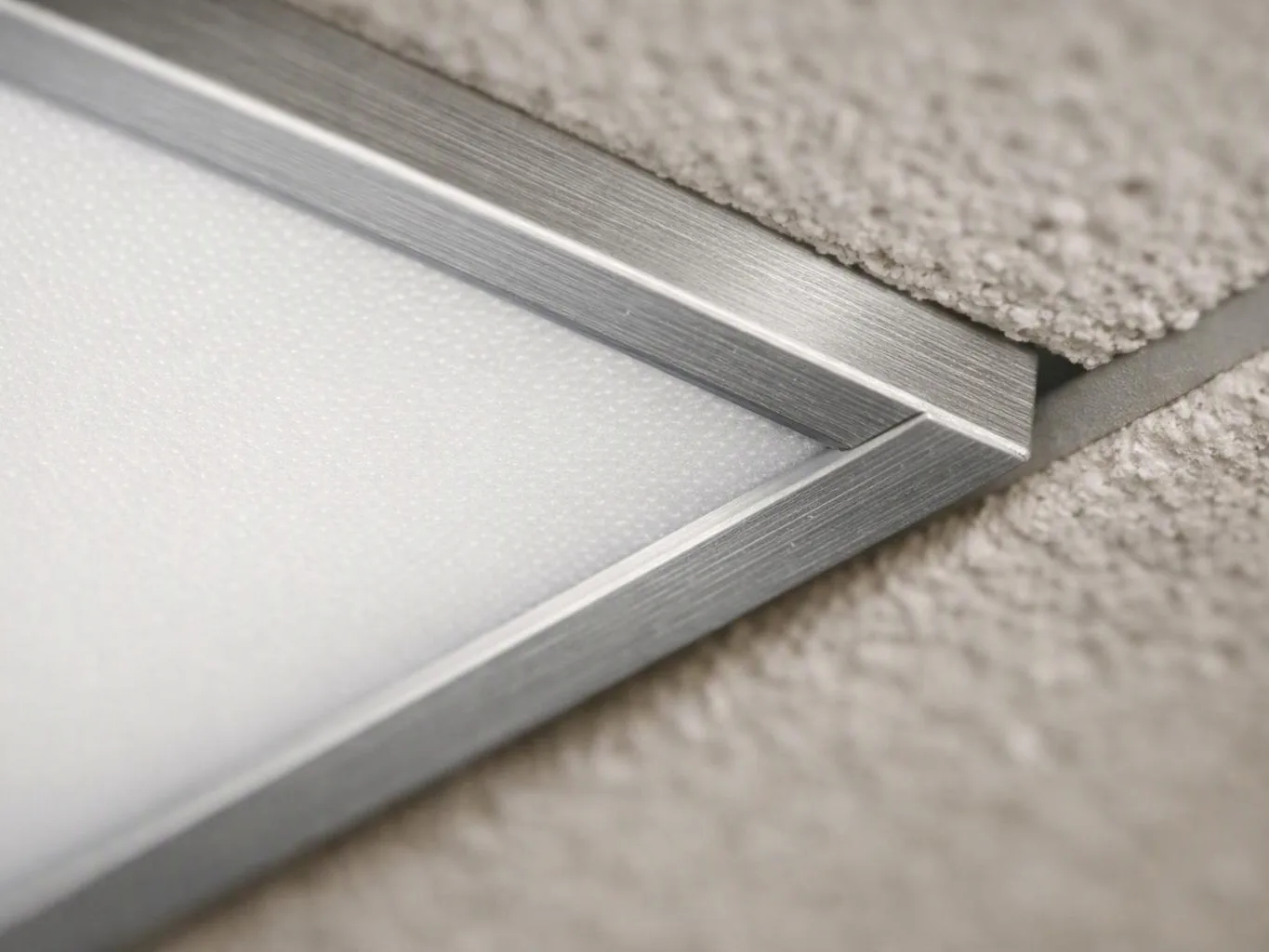Close-up of a silver metal frame holding a frosted panel against a textured beige wall