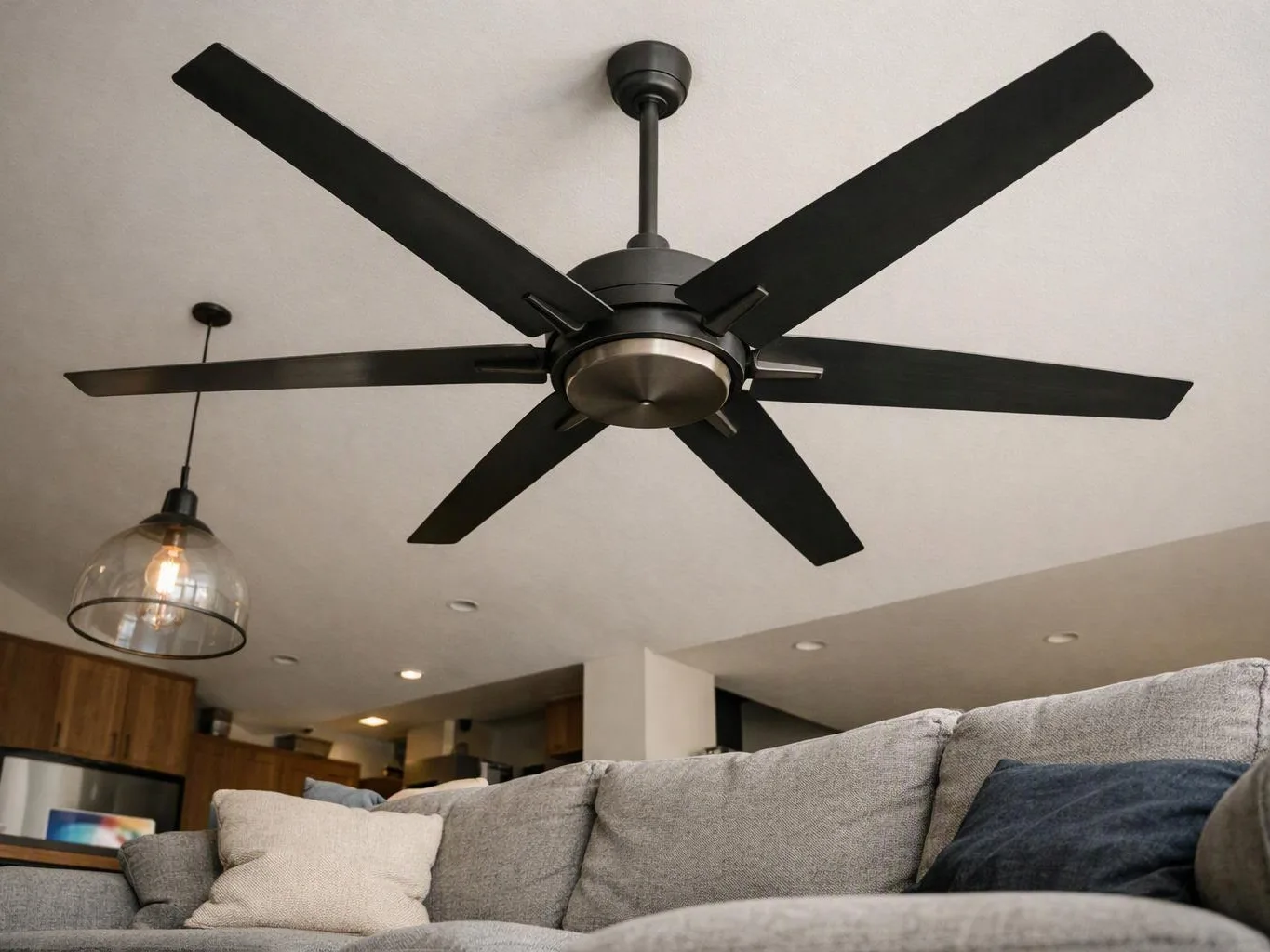 A large black ceiling fan hangs above a gray sofa in a modern living room